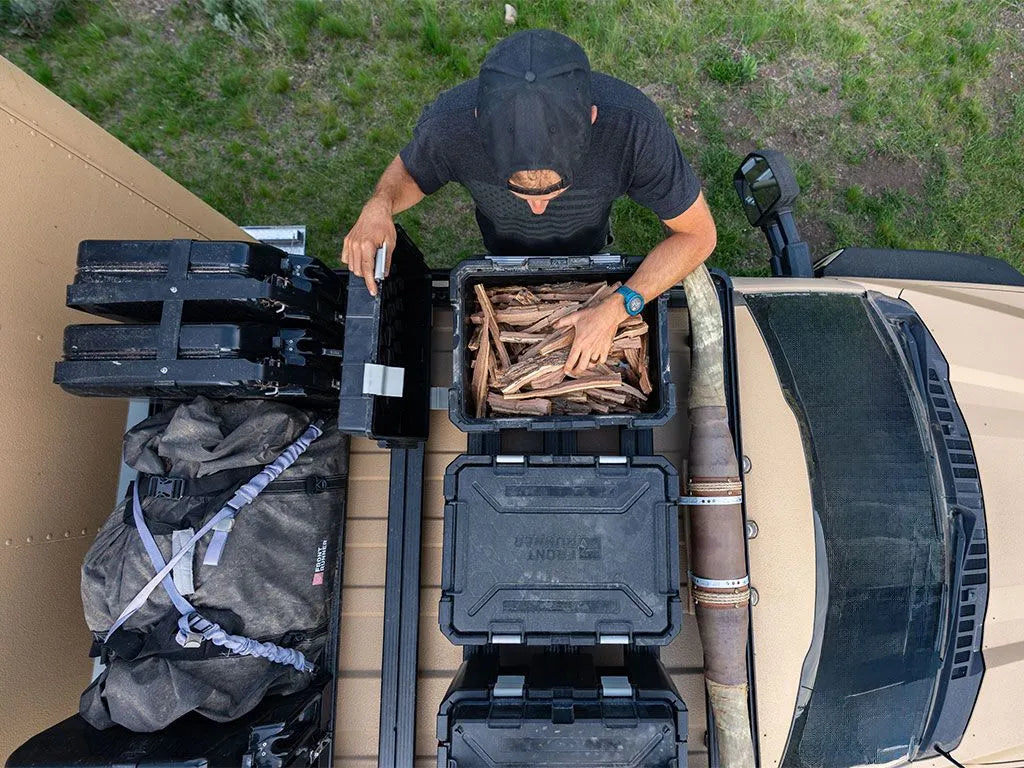 Person loading wood into a black storage bin on a vehicle's roof rack.