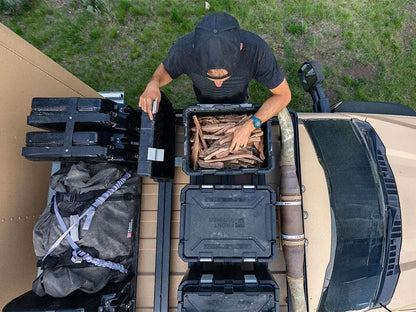 Person loading wood into a black storage bin on a vehicle's roof rack.
